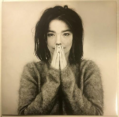 Photo of a young Bjork in a fuzzy sweater with hands pressed together in front of her mouth.