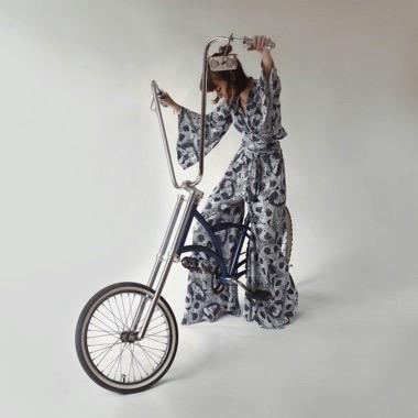 Person in a patterned outfit standing next to a unicycle on a plain background