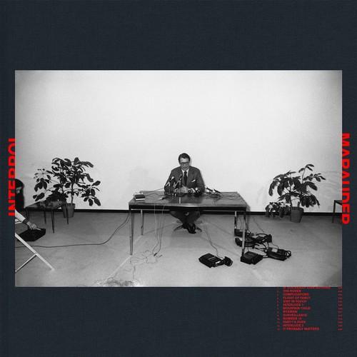 Black and white album cover featuring a person sitting at a desk with a microphone, flanked by two potted plants.