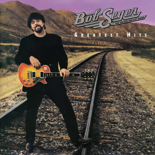 cover feature Bob Seger standing on railroad tracks in the desert holding an orange guitar