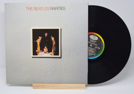 The image shows a vinyl record titled 'The Beatles - Rarities' placed in its cover sleeve, with a wooden record holder underneath.