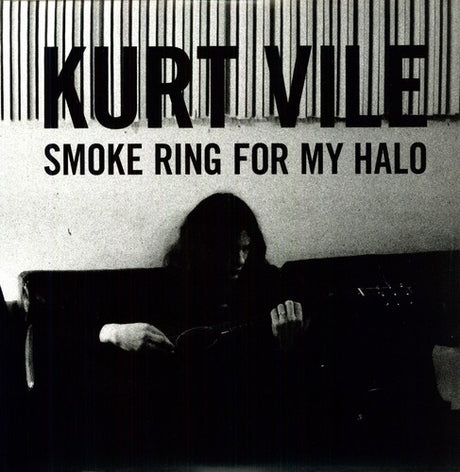 The image features Kurt Vile, the artist behind the album 'Smoke Ring For My Halo'. He is seated, playing an instrument, with a dark backdrop that has the title 'KURT VILE SMOKE RING FOR MY HALO' printed at the top.